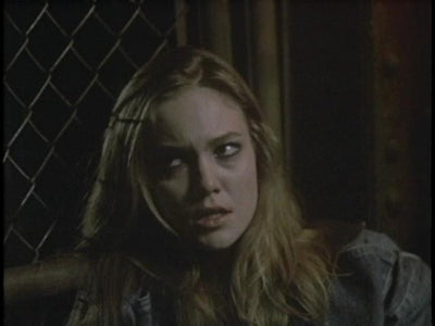 A worried woman looks to one side beside a wire-mesh window in Lady Beware (1987).