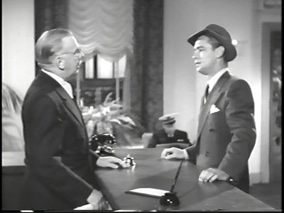 A man in a hat speaking with another man across a reception desk in The Blue Dahlia.