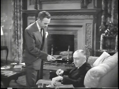 A standing man beside a seated man and an ornate fireplace in The Blue Dahlia.